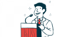 A man, wearing a tie and jacket, speaks into a microphone at a podium.